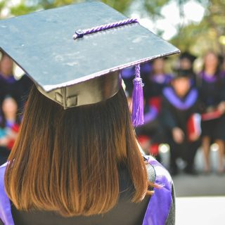 A graduate in a cap and gown seen from behind at a ceremony