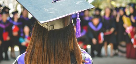 A graduate in a cap and gown seen from behind at a ceremony
