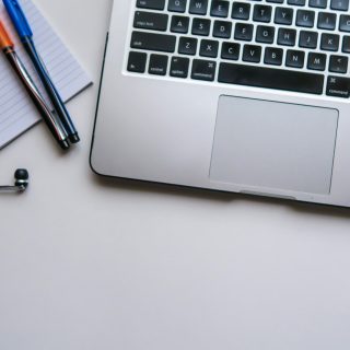 A laptop beside a notebook, pens and earphones on a desk