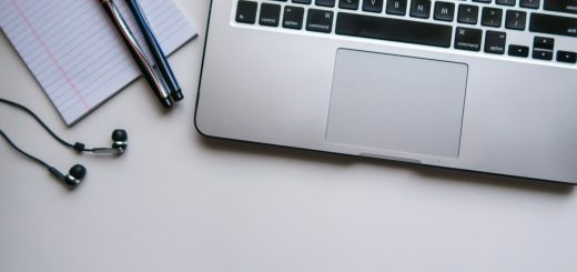 A laptop beside a notebook, pens and earphones on a desk
