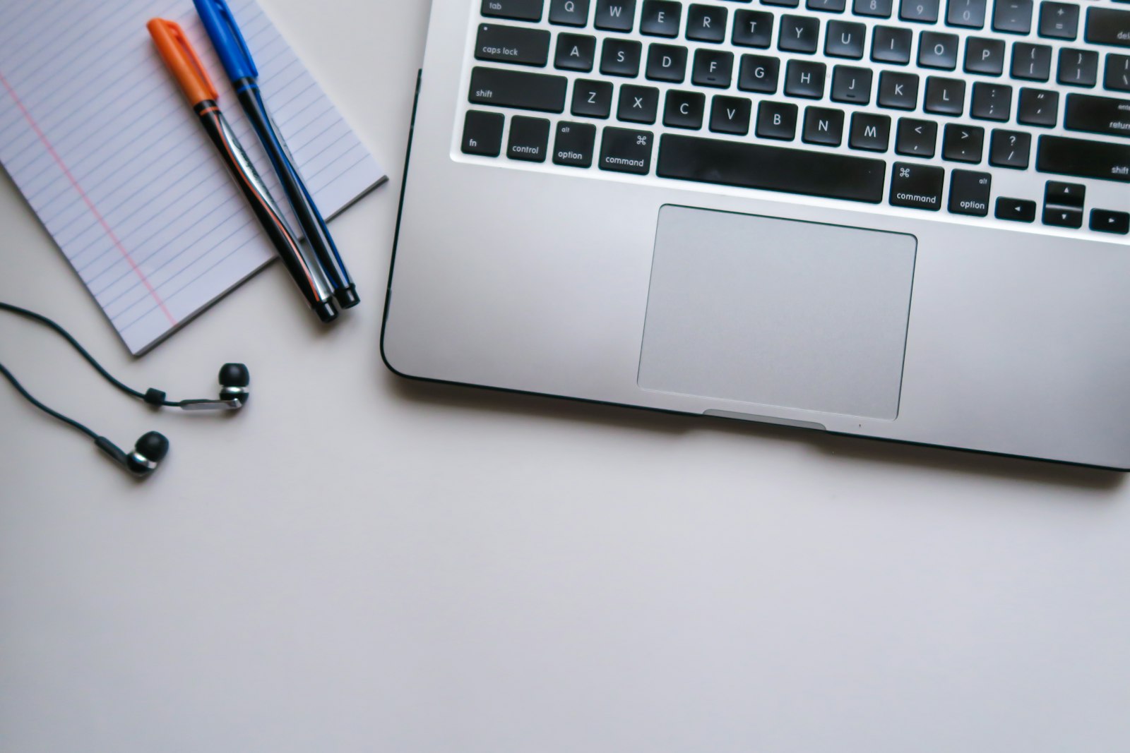 A laptop beside a notebook, pens and earphones on a desk