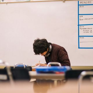 A student writing at a desk in a classroom