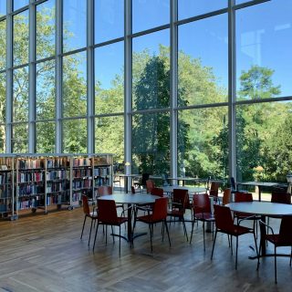A bright library with tall windows, bookshelves and study tables
