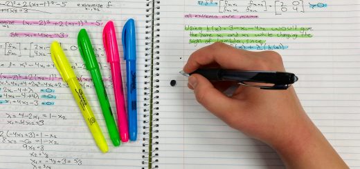 A hand writing notes in a notebook beside colourful highlighters