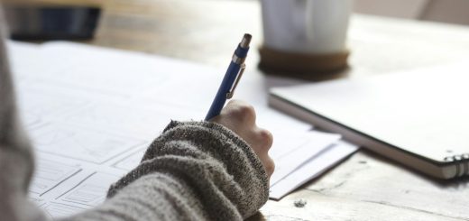 A person writing notes at a wooden table beside a mug